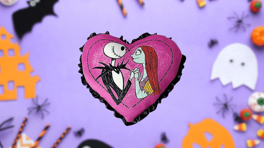 Heart-shaped pillow featuring Jack Skellington and Sally from The Nightmare Before Christmas, with a pink background and black ruffled trim.