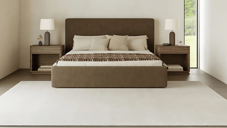 Minimalist bedroom with a brown upholstered bed, beige bedding, two wooden nightstands with matching table lamps, and a large white area rug.