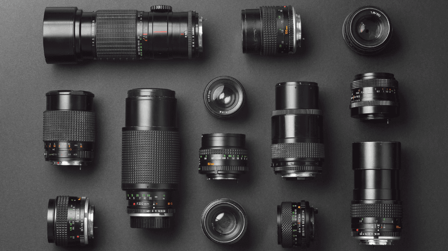 A collection of various camera lenses arranged neatly on a dark surface, showcasing different sizes and focal lengths, including telephoto, wide-angle, and prime lenses.