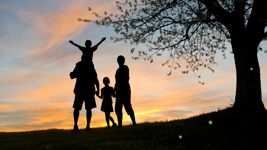 Silhouette of a family with two children enjoying sunset outdoors, one child on an adult's shoulders, under a blossoming tree.