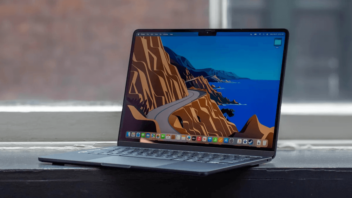 Open laptop with a colorful coastal wallpaper displayed on the screen, placed on a windowsill.