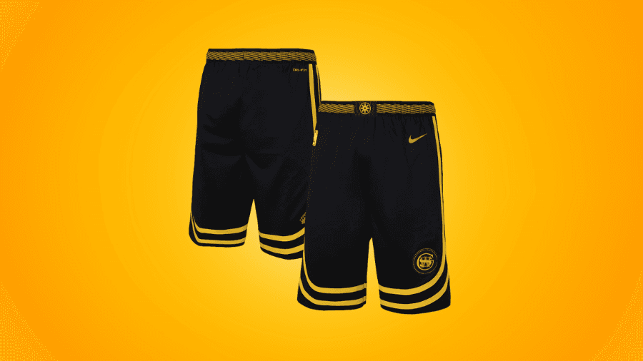 Black Golden State Warriors basketball shorts with yellow accents, featuring a woven waistband and team logo, displayed against an orange background.