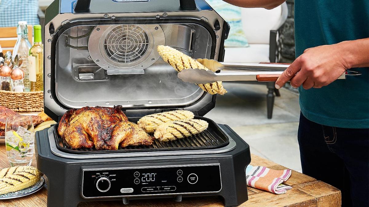 Grilled chicken and corn cooking on a Ninja Woodfire Pro XL electric outdoor grill with the lid open.