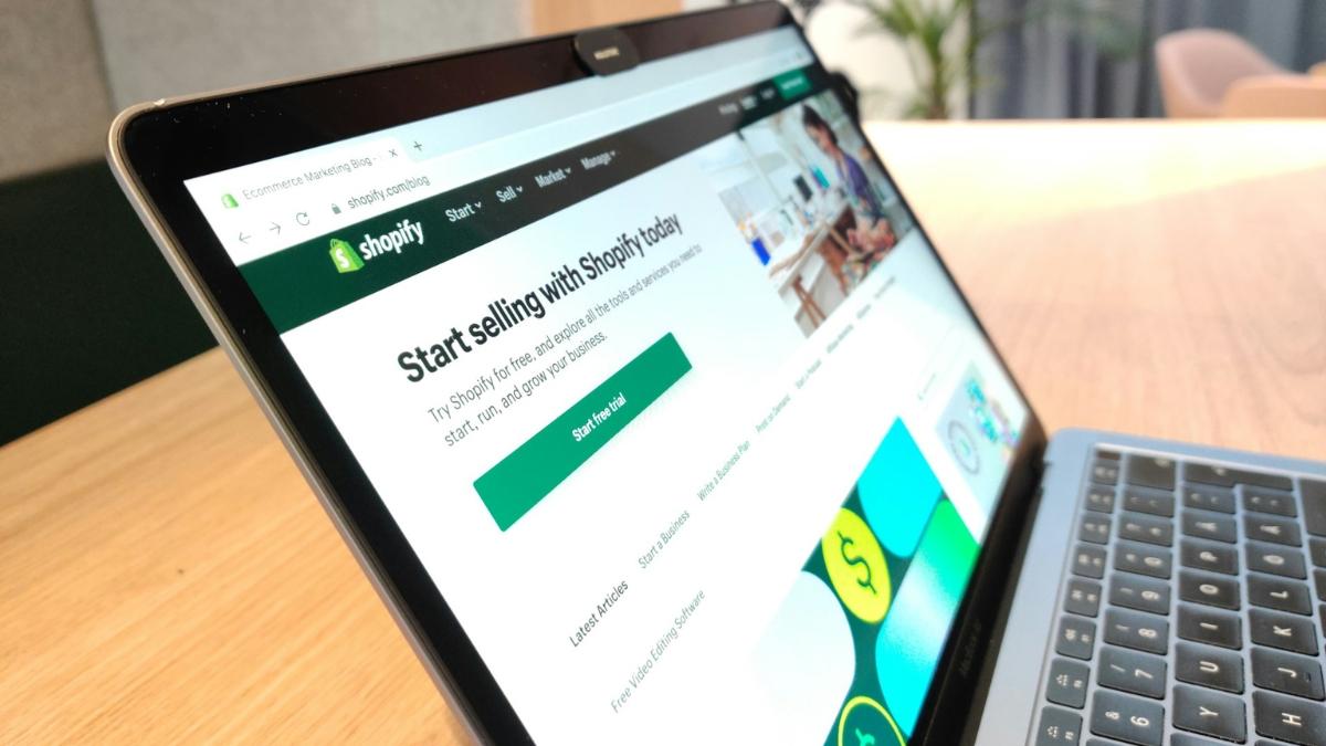 A laptop screen showing the Shopify blog homepage with a green button to start a free trial.