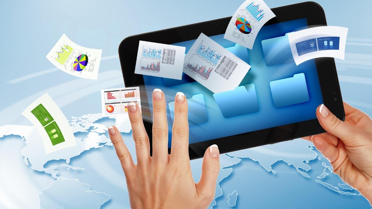 Hands holding a tablet with digital folders and colorful data charts floating above a world map.