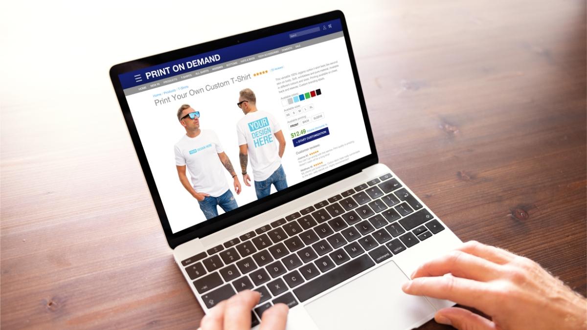 Person using a laptop to design a custom print-on-demand T-shirt on an online store.