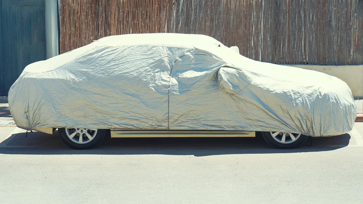 A parked car is fully covered with a silver car cover to protect it from sun and dust.