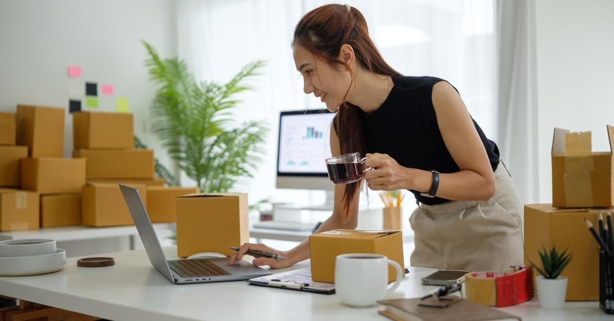 Small business owner packing online orders at desk with laptop and shipping boxes